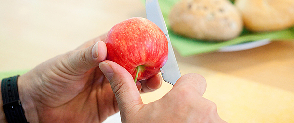 Die Hände eines Patienten, der mit einem Messer einen Apfel halbiert.